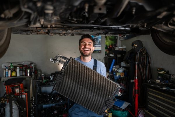 car mechanic happily holding car radiator part in garage