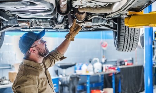 Professional,Caucasian,Mechanic,Standing,Under,The,Vehicle,Lifted,On,Car